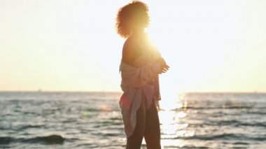 Genç Afrikalı pozitif iyimser kadın mayo giyip plajda dans ediyor.