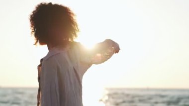 Mayolu genç Afrikalı bir kadın sahilde dans ediyor.