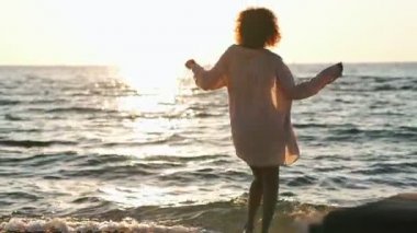 Genç Afrikalı pozitif iyimser kadın mayo giyip plajda dans ediyor.