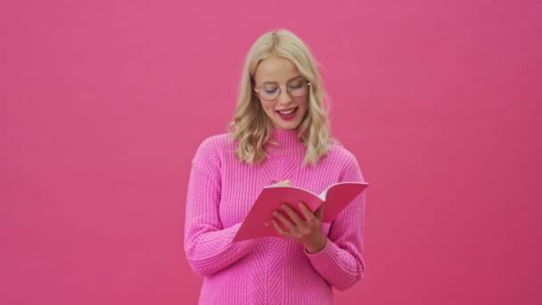 분홍색 스웨터를 아름다운 금발의 여성이 자신의 노트를 — 비디오