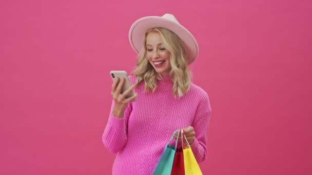 Uśmiechnięta Blondynka Różowym Swetrze Trzyma Kolorowe Torby Zakupy Różowym Tle — Wideo stockowe