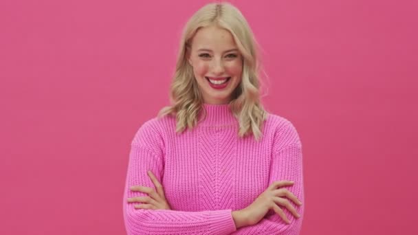 一位穿着粉色毛衣 面带微笑的金发女人 在粉色背景下孤零零地站着打盹 — 图库视频影像