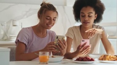 İki güzel kadın sabah kahvaltıda akıllı telefonlarını kullanıyorlar.