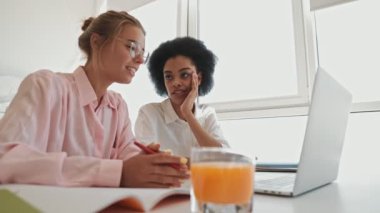 İki pozitif kadın evdeki masada dizüstü bilgisayar kullanıyor.