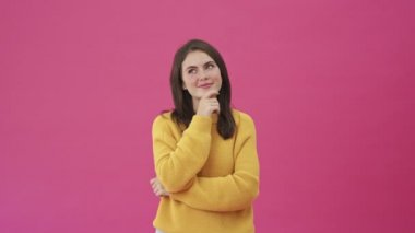 Sarı kazaklı güzel bir kadın pembe arka planda tek başına ayakta duruyor.