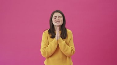 Sarı kazaklı hoş bir kadın pembe arka planda tek başına dua ederken bir şey istiyor.