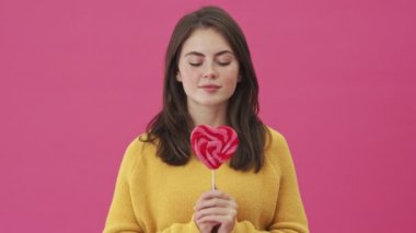 Gülümseyen bir kadın pembe arka planda izole bir şekilde duran bir lolipop tutuyor.