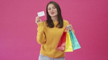 Gülümseyen bir kadın pembe bir arka planda tek başına duran renkli cepler ve kredi kartı taşıyor.