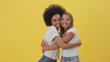 Gülümseyen kadınlar birbirlerine sarılıyorlar. Sarı arka planda tek başlarına duruyorlar.