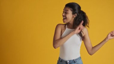 Oyuncu genç bir kadın sarı arka planda tek başına duran boş alana işaret ediyor.