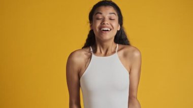 Memnun bir genç kadın kameraya bakarken, sarı arka planda tek başına duran iltifatları dinliyor.