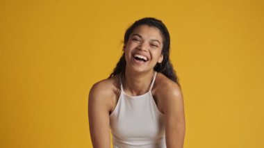 Çekici bir genç kadın gülüyor ve sarı arka planda tek başına kameraya bakıyor.