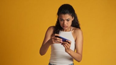 Odaklanmış genç bir kadın, sarı arka planda tek başına duran akıllı telefonuyla oyunu kazanıyor.