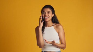 Güzel genç bir kadın, sarı arka planda tek başına duran akıllı telefonuyla konuşuyor.