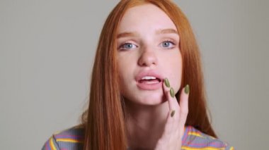 Beyaz duvar arkasında izole edilmiş genç, pozitif saçlı kadın aynadaki gibi kameraya bakıyor.