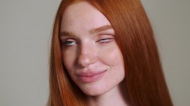 Genç, güzel, kızıl saçlı, neşeli kadın beyaz duvar arkasında yalnız poz veriyor.