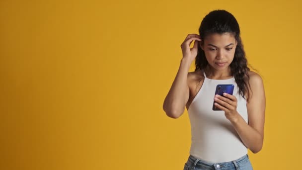 Gülümseyen Genç Bir Kadın Akıllı Telefonunu Kullanıyor Sarı Arka Planda — Stok video