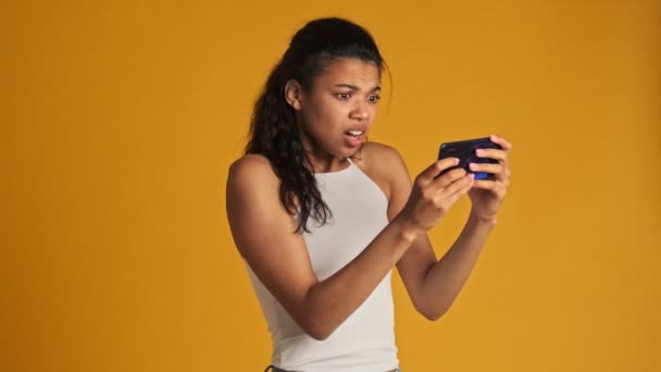 一位吓坏了的年轻女子正在智能手机上观看恐怖的视频 她将视频水平地放在黄色背景上 与外界隔绝 — 图库视频影像