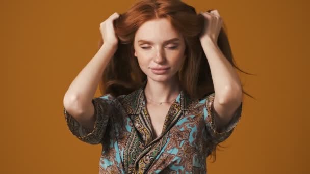 魅力的な若い女性はポーズをとっている間に彼女の髪を横に振っている茶色の背景 — ストック動画