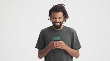 Genç Afrikalı mutlu olumlu adam cep telefonu kullanarak beyaz duvar arkaplanı üzerinde izole
