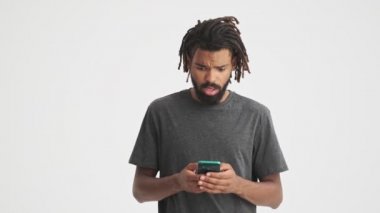 Genç afrikalı şaşkın adam beyaz duvar arkaplanı üzerinde cep telefonu kullanarak izole