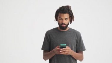 Genç Afrikalı şok olmuş bir adam cep telefonu kullanarak beyaz duvar arkasında izole edilmiş.