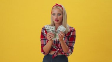 Şaşırmış genç bir kadın, sarı arka planda tek başına duran parasını sayıyor.
