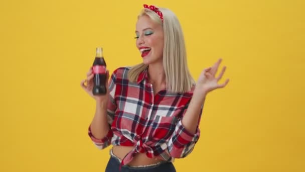 一个爱开玩笑的年轻女子正在一个被黄色背景隔开的玻璃瓶里喝可乐 — 图库视频影像