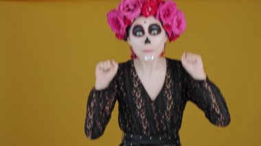 Karnaval kostümü giymiş çekici bir kadın sarı arka planda elini sallayarak zıplıyor.