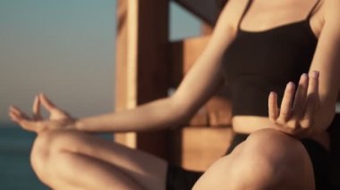 Genç bir kadının kırpılmış görüntüsü sabahleyin plajdaki oyuğun yanında yoga yapıyor.