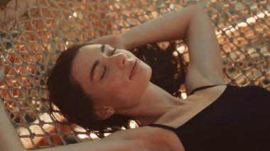 Genç ve güzel bir kadın sabah suyun üstündeki hamakta uyuyor.