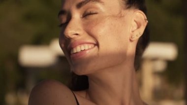 Mutlu genç bir kadının yakın çekim görüntüsü sabahın köründe yoga minderiyle dışarıda duruyor.