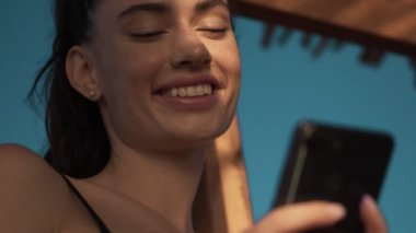 Mutlu genç bir kadının yakın plan görüntüsü sabah sahilde dururken akıllı telefonunu kullanıyor.