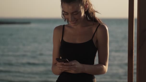 Усміхнена Молода Жінка Використовує Свій Смартфон Стоїть Пляжі Вранці — стокове відео