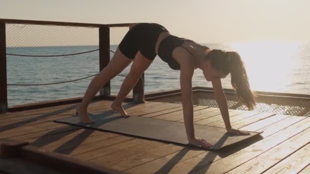 一位年轻的女运动员正在海滩上的瑜伽垫上做伸展运动 — 图库视频影像