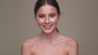 Sağlıklı ciltli, genç, güzel, mutlu bir kadın. Gri duvar arkasında yalnız poz veriyor.