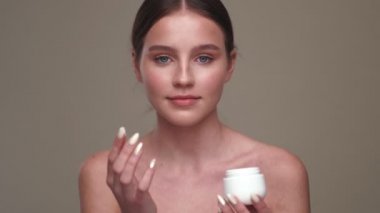 Sağlıklı ciltli, gri duvar arkasında izole edilmiş krem ile poz veren genç, mutlu, pozitif kız.