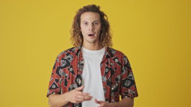 Şok olmuş genç bir adam sarı arka planda tek başına ağzını açıyor.