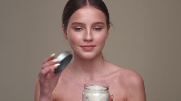 Νεαρό Χαμογελαστό Κορίτσι Υγιές Δέρμα Ποζάρουν Κρέμα Απομονώνονται Γκρι Φόντο — Αρχείο Βίντεο