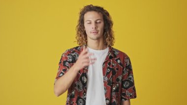 Hayal kırıklığına uğramış genç bir adam sarı arka planda tek başına dururken avuç içi hareketi yapıyor.