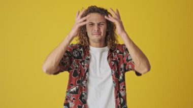 Şok olmuş genç bir adam sarı arka planda tek başına başını tutuyor.