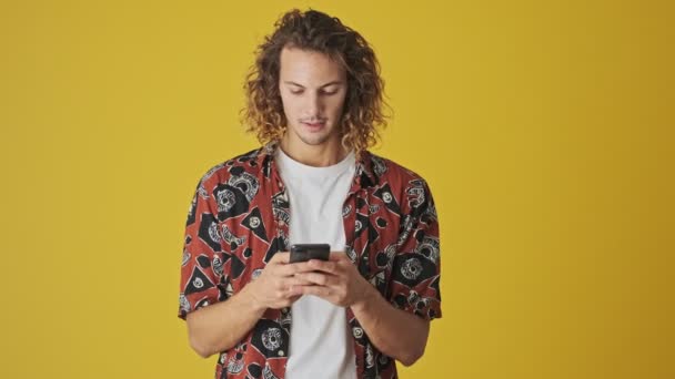 Poważny Młody Człowiek Używa Swojego Smartfona Stojącego Żółtym Tle — Wideo stockowe