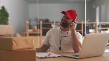 Ofisteki genç mutlu posta müdürü, paket kutularının yanında müşteriyle konuşuyor.