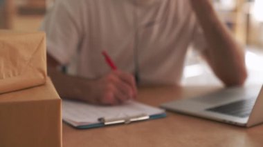 Genç memnun posta müdürü ofiste müşteriyle konuşuyor ve paket kutularının yanına notlar yazıyor.