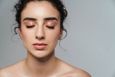 Gri duvarın üzerinde gözleri kapalı poz veren güzel yarı çıplak bir kadın resmi.