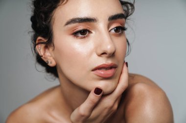 Güzel, yarı çıplak, kıvırcık saçlı bir kadın görüntüsü. Gri duvarın diğer tarafına bakıyor ve poz veriyor.