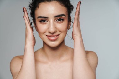 Gülümseyen yarı çıplak bir kadın resmi. Gri duvarın üzerinde elleri kusmuş poz veriyor.