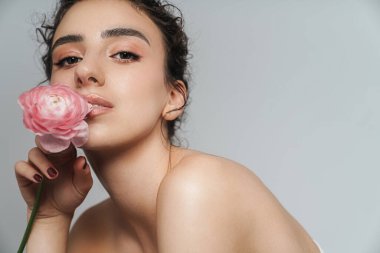 Gri duvarın üzerinde pembe çiçekle poz veren çekici yarı çıplak kadın.