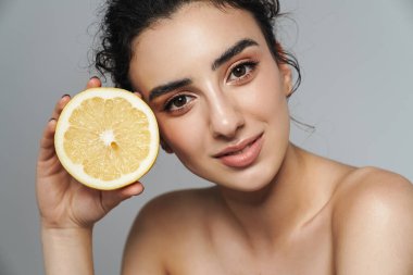 Gri duvarın üzerinde limonla poz verirken yarı çıplak bir kadının baştan çıkarıcı görüntüsü.