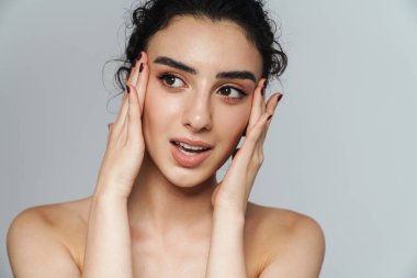 Güzel, yarı çıplak, kıvırcık saçlı bir kadın görüntüsü. Gri duvarın diğer tarafına bakıyor ve poz veriyor.